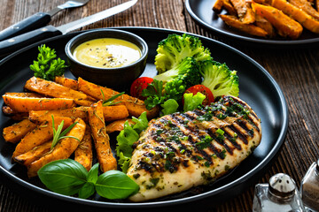 Grilled chicken breast, sweet potato fries with barbecue sauce and boiled broccoli on wooden table
