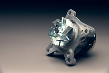 A new, shiny aluminum engine coolant pump on a gray gradient background. Contrast backlighting.