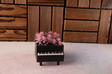 Miniature Black Piano With Pink Flowers In Box On Wooden Floor Studio Scene