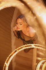 Sexy blond model alluring in bright dress in royal luxury interior with golden chandelier