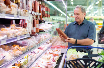 Elderly man chooses sausage in supermarket