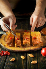 Hands skillfully portion a sweet dessert on a wooden board. Viburnum berry toppings and almonds are arranged around the treat, creating an inviting presentation