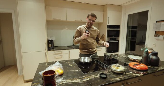 A man stands in the kitchen stirring food while staring at his smartphone, symbolizing distraction, social media overuse, multitasking, and reduced attention during cooking.