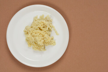 An overhead studio shot shows a pile of freshly grated ginger on a small white plate, set against a neutral brown background with copy space