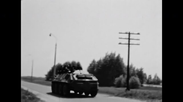 Soldiers driving in tank by rural road. War. Army troops riding on top of military armored personnel carrier moving by paved street. Armed conflict. Old film. Archival retro 1960s. Vintage archive