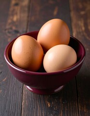 3 brown eggs in a bordeaux ceramic bowl on wooden table
