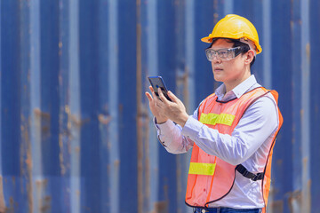 Professional Asian man worker in port cargo shipping industry using smartphone technology for work