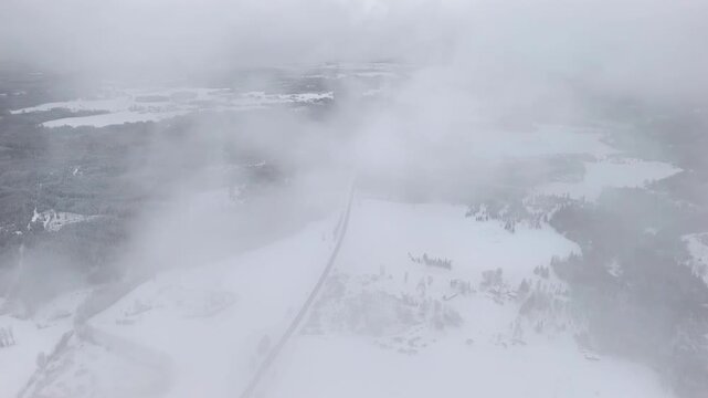 High drone shot with camera panning over a snowy landscape, with moving clouds passing in front of the view and a road crossing the scene.