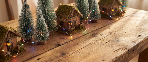 Rustic wooden table decorated with miniature houses, evergreen trees, and colorful fairy lights creating a cozy winter holiday scene
