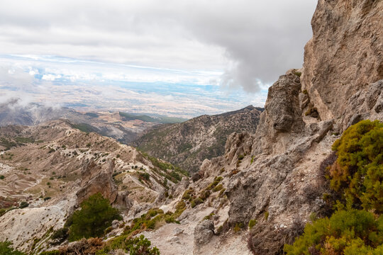 Rugged limestone cliffs and steep slopes descend into deep valleys under dramatic cloudy skies, capturing the raw beauty of the mountainous landscape in Sierra Nevada National Park near Monachil.
