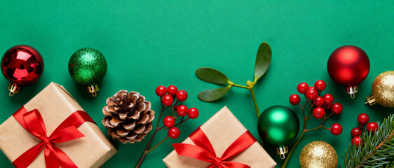 Festive christmas background with gift boxes, pine cones, red berries, baubles, mistletoe, and evergreen branches on green