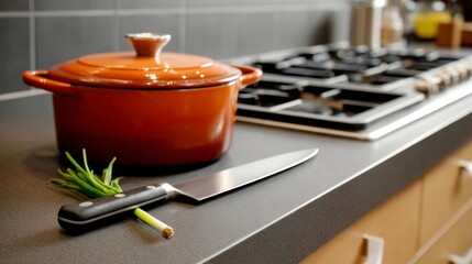 Kitchen countertop featuring a vibrant orange cooking pot, a sharp knife, and fresh green onions, creating an inviting culinary atmosphere for food preparation and cooking