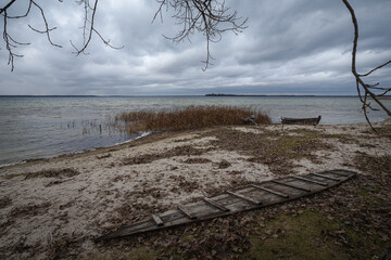 Old rural wooden, fishing boat is moored on the shore of a lake. A gloomy windy day