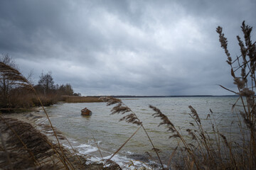 Old rural wooden, fishing boat is moored on the shore of a lake. A gloomy windy day
