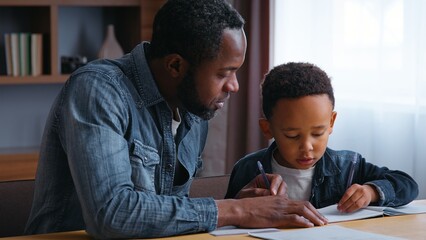 African American family dad assists son with learning teamwork lovely schoolboy with father writing homework at home child kid boy with parent tutor tutoring distant education concentration study