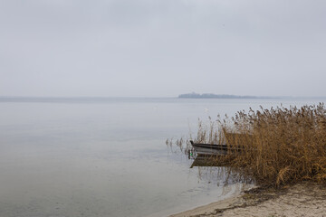 Old rural wooden, fishing boat is moored on the shore of a lake. A gloomy windy day