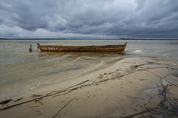 Old rural wooden, fishing boat is moored on the shore of a lake. A gloomy windy day