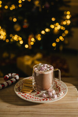 Holiday, Christmas background. A cup with hot chocolate and marshmallows on the table with Christmas tree on background