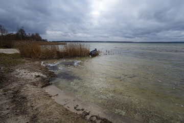 Old rural wooden, fishing boat is moored on the shore of a lake. A gloomy windy day