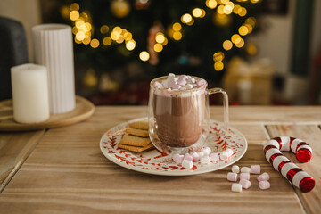 Holiday, Christmas background. A cup with hot chocolate and marshmallows on the table with Christmas tree on background