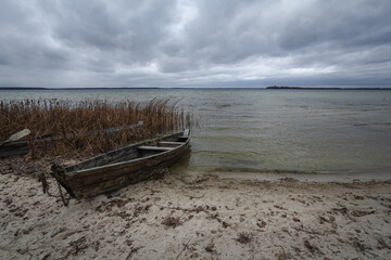 Old rural wooden, fishing boat is moored on the shore of a lake. A gloomy windy day