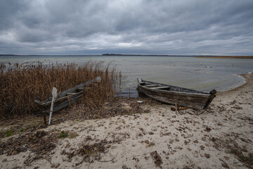 Old rural wooden, fishing boat is moored on the shore of a lake. A gloomy windy day
