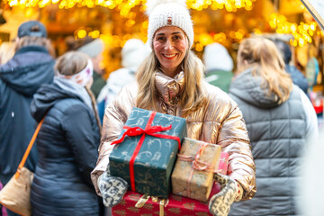 Smiling woman with Christmas gifts at a Bavarian market in Germany enjoying warm festive lights and winter charm