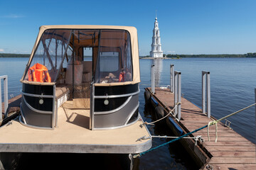 A landscape with the flooded bell tower of St. Nicholas Cathedral in the town of Kalyazin on the Volga River and tourist boats waiting for tourists at the pier