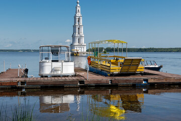 A landscape with the flooded bell tower of St. Nicholas Cathedral in the town of Kalyazin on the Volga River and tourist boats waiting for tourists at the pier
