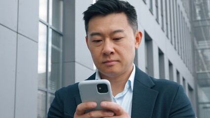 Pensive Asian Korean business man with mobile phone thinking typing message middle-aged Korean businessman in city deciding think idea browsing chatting smartphone app Japanese Chinese male worker