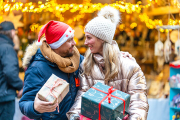 Happy couple at a Bavarian Christmas market carrying festive gifts while enjoying warm holiday lights