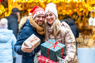 Joyful couple embracing holiday cheer at a Bavarian Christmas market holding bright festive presents
