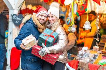 Couple holding Christmas gifts while exploring a Bavarian market filled with lights festive decor and winter charm