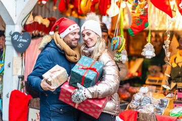 Couple celebrating winter magic at a Bavarian Christmas market holding colorful gifts and sharing festive joy