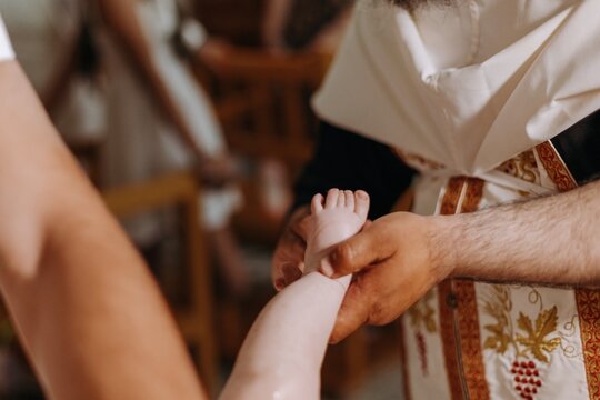 Priest's hands holding a baby's bare foot during the anointing ritual of an Orthodox baptism ceremony in a church