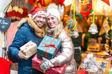Couple enjoying winter romance at a Bavarian Christmas market holding colorful gifts under glowing lights
