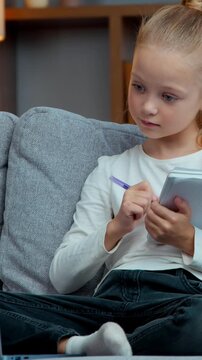 Caucasian clever pupil kid child girl daughter concentrated learn studying with e-learning web course on couch writing notes raising hand answer to teacher study learning with laptop at evening home