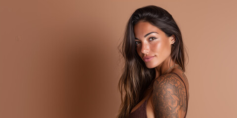 Woman with long brown hair and tattoo poses against a simple warm background in a relaxed indoor setting during the day