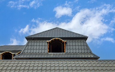 House with a black roof and a blue sky. The roof is slanted and has a window