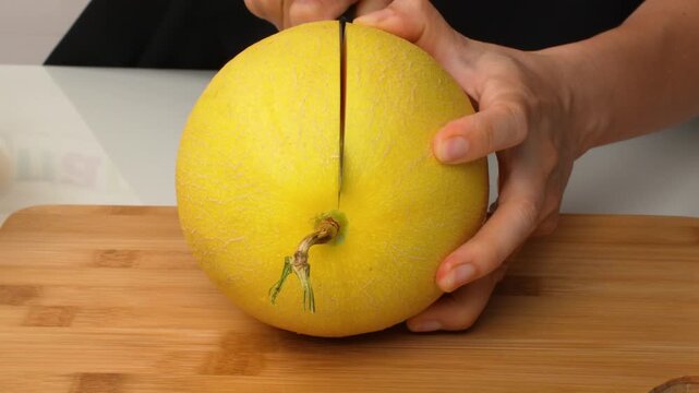 Woman cutting yellow netted melon on wooden board. Female hands slicing fresh fruit with knife. Healthy food concept.