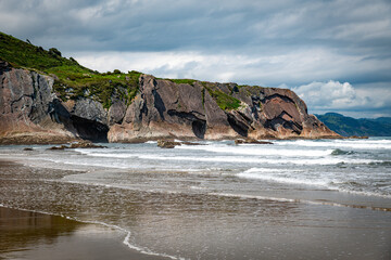 Dramatic Coastal Cliffs By The Sea With Waves, Soft Sand Beach and Green Hills