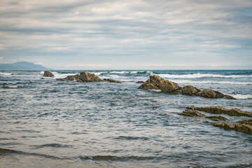 Coastal Beach With Rocky Outcrops and Cliffside Shoreline Under Cloudy Sky