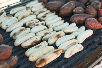 Delicious grilled banana and roasted sweet potato, traditional street food snack. warm, healthy dessert cooking on charcoal grill at an outdoor barbecue market