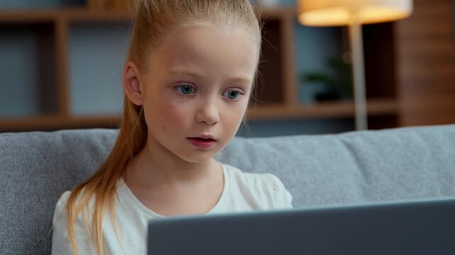 Concentrated Caucasian child girl typing laptop at home focused little kid daughter pupil schoolgirl user studying with computer distant education playing at cyberspace communicate in internet chat