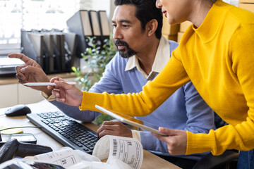 Small business couple analyzing printed labels, recording shipment updates by computer technology, coordinating inventory tasks, e-commerce operations with teamwork, and organizing warehouse planning