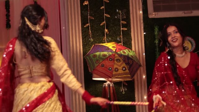 Girls playing Garba Dandiya in traditional red and golden lehenga during festive indoor celebration