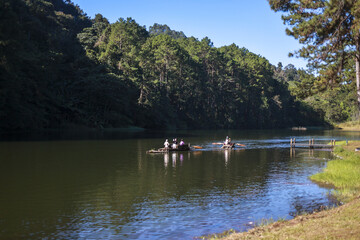 Tranquil scene of bamboo raft with tourists floating on serene lake. peaceful water reflects blue sky and green forest on sunny day of outdoor adventure travel