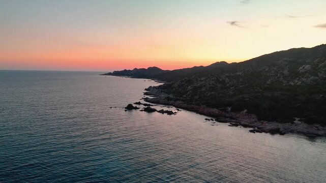 Low Aerial Drone Flight Over Rugged Capu di Fenu Coastline Towards the Setting Sun, Illuminating Rocky Cliffs and Mediterranean Sea, Corsica, France.