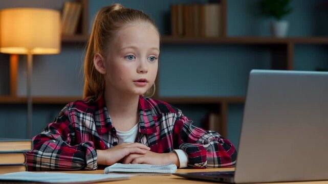 Serious Caucasian kid child girl talking video call with laptop in evening home daughter school pupil studying online distant talk communicate with teacher in conference web class remote education