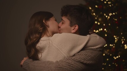 A tender holiday moment as a reunited couple shares a warm kiss and tight embrace after being apart, while the camera pulls back to reveal glowing decorations and a Christmas tree around them.